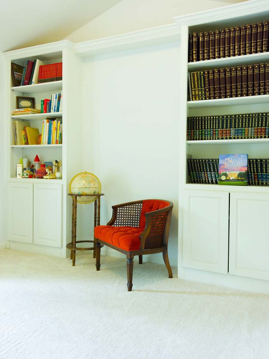 shelf red padded brown wooden armchair beside white wooden shelf bookcase