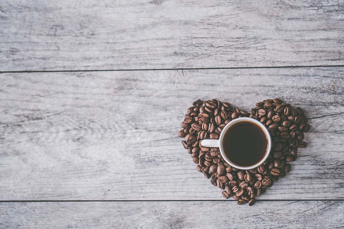 coffee coffee filled white ceramic mug beside brown coffee beans on beige wooden surface grey