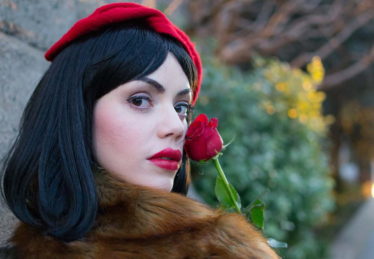person woman wearing brown coat holding red rose near wall during daytime people