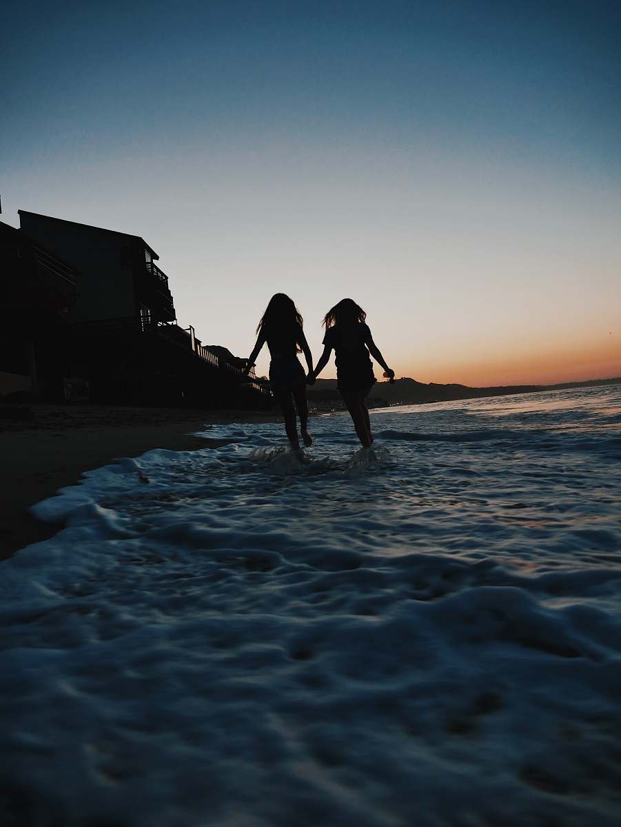 coast silhouette of two women running across seashore beach