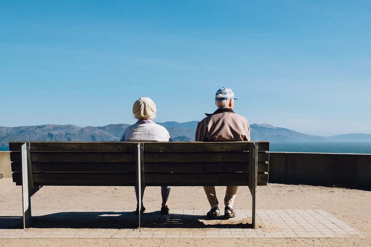 person man and woman sitting on bench facing sea bench