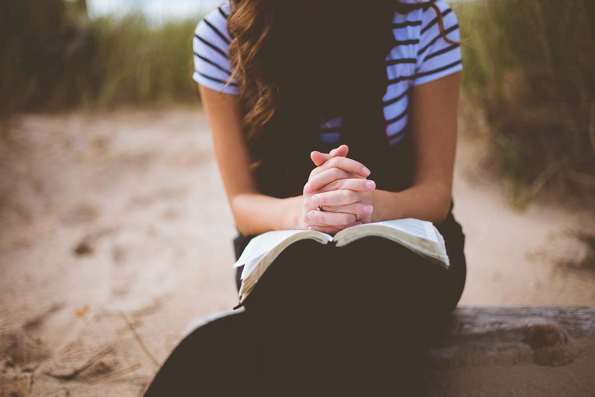 person woman sitting on brown bench while reading book prayer
