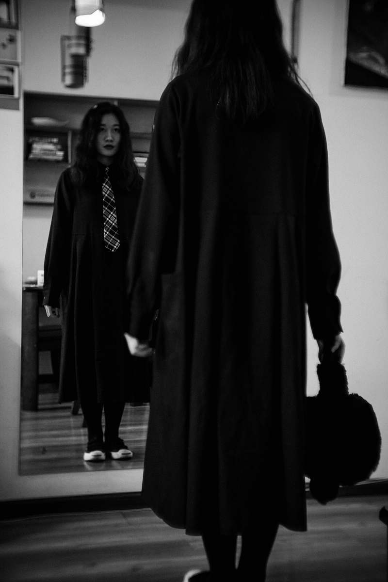clothing woman wearing black coat facing mirror apparel
