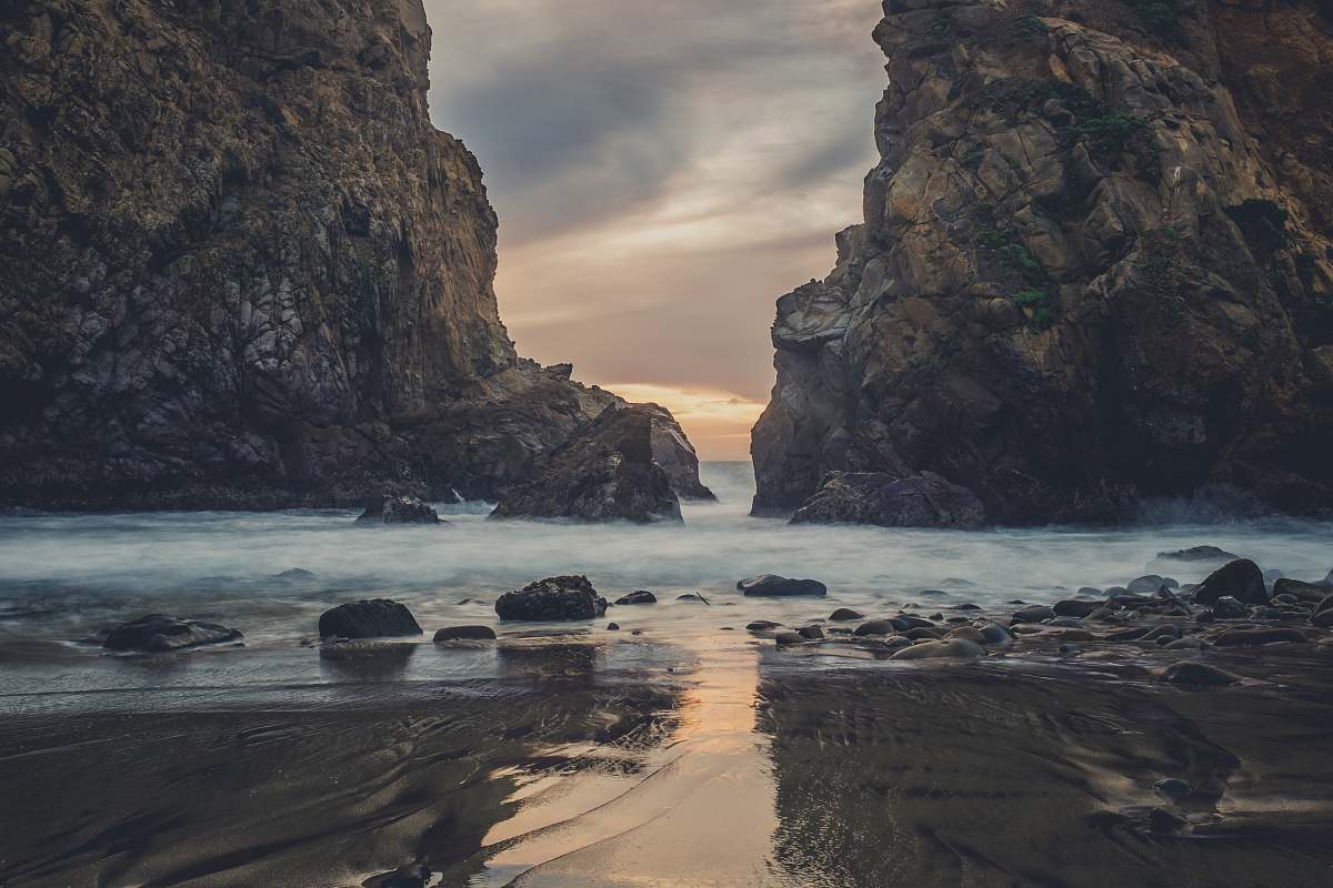 Capture the mesmerizing beauty of nature with this stunning wallpaper featuring a river overflow nestled between dramatic rock formations. The scene is illuminated by a breathtaking sunset, casting warm hues over the rocky beach and tranquil waters. Perfect for nature enthusiasts, travel blogs, or as a serene backdrop for any digital project, this image encapsulates the harmony of land and water, inviting viewers to immerse themselves in its serene beauty.