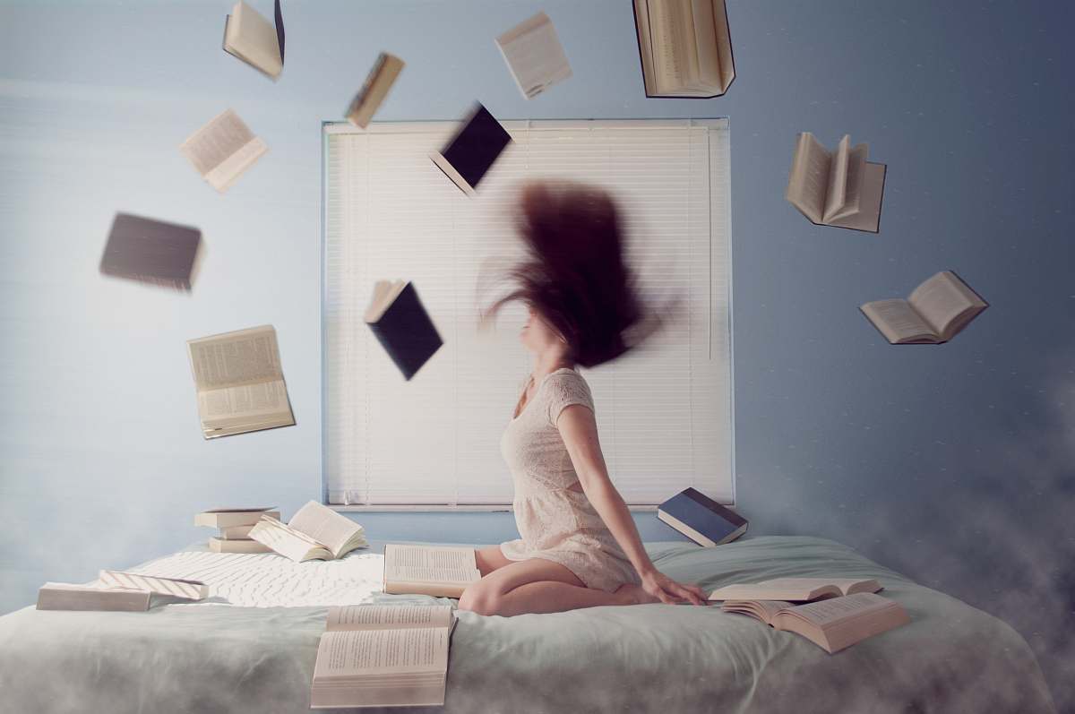 books woman sitting on bed with flying books girl