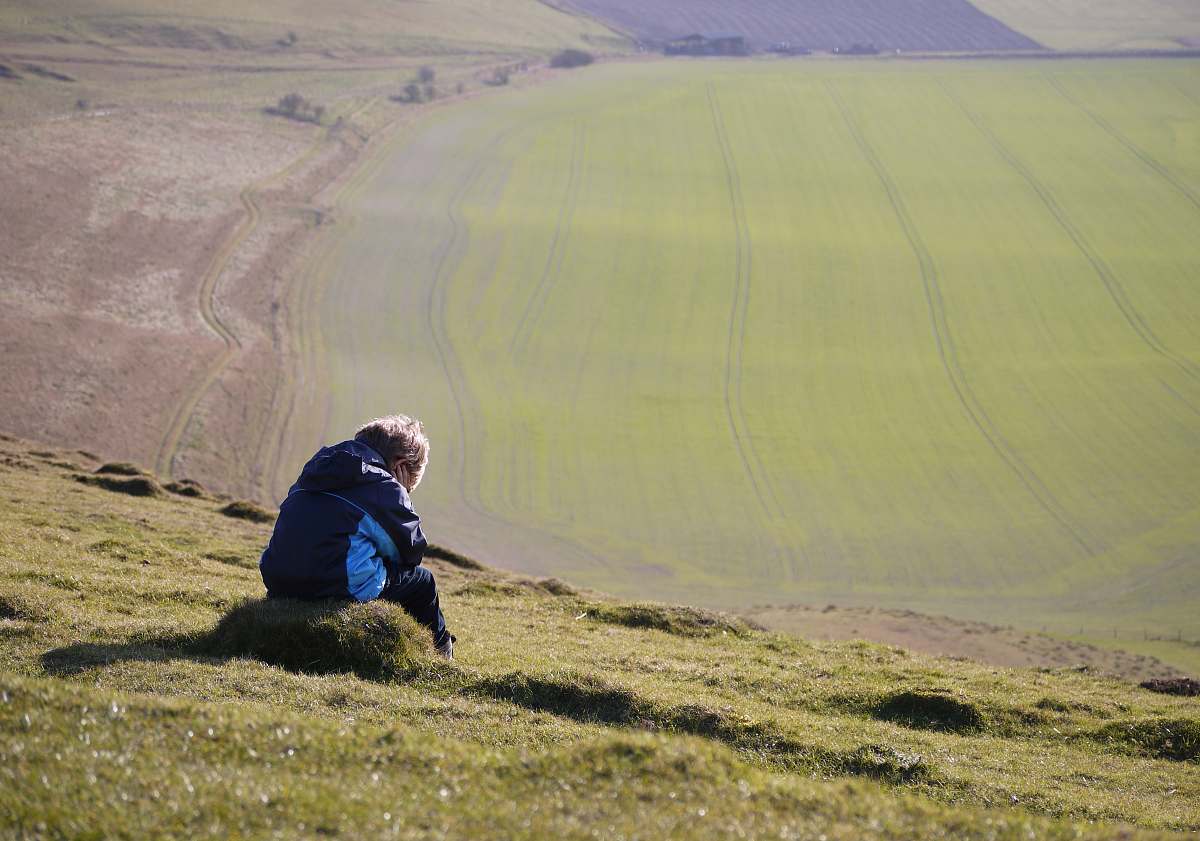 person man sitting on green grass looking on green mountains outdoors