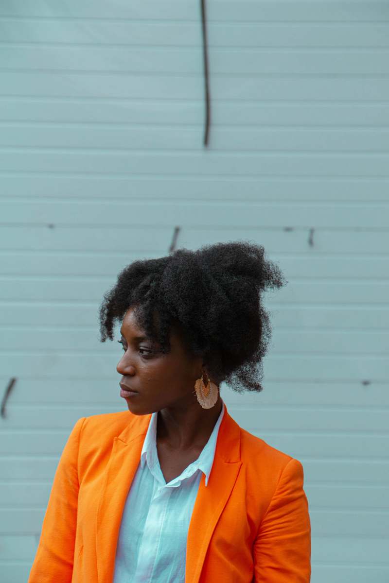 person woman wearing orange blazer standing near white wall hair