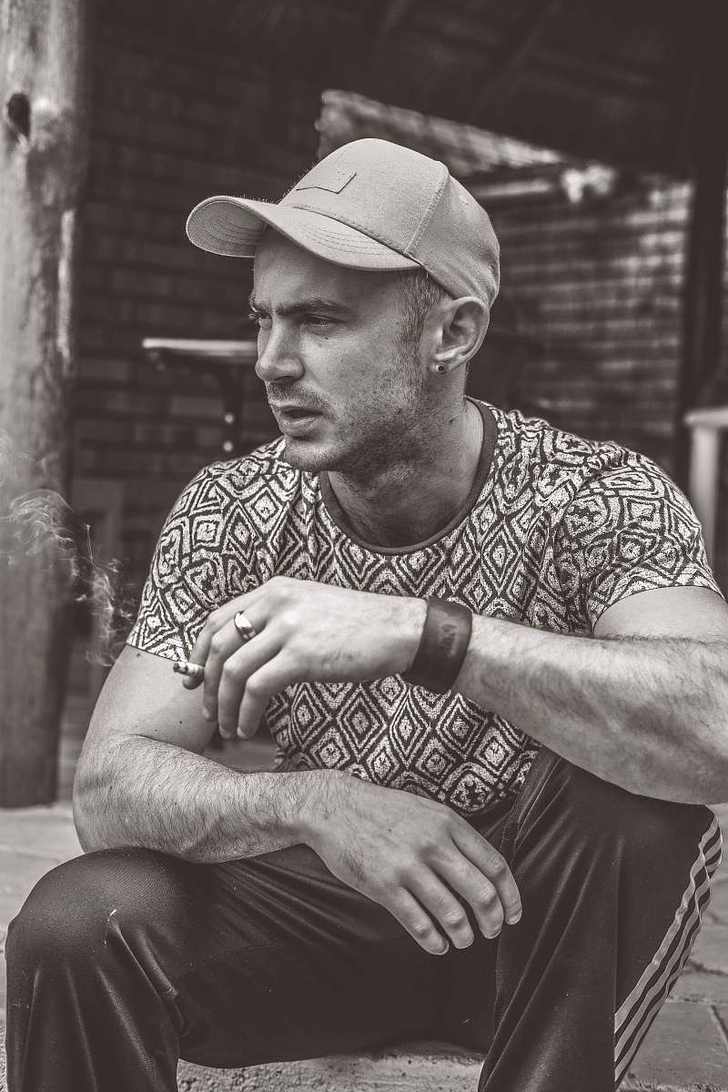 human grayscale photo of man sitting on holding cigarette stick people