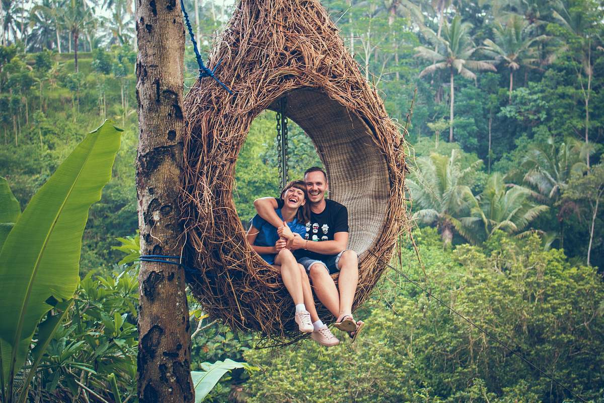 human man and woman riding on brown hammock beside brown tree people
