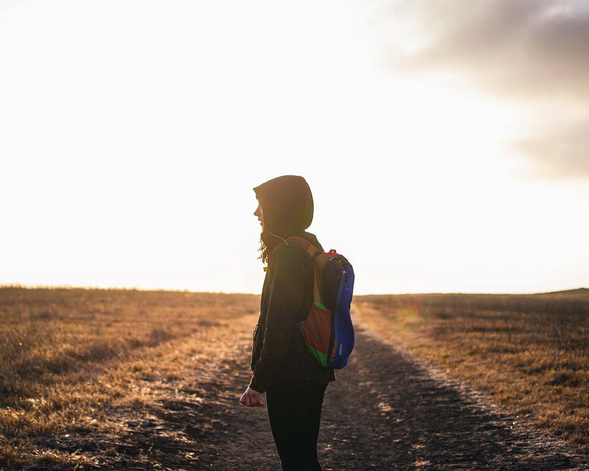 human person wearing backpack standing on pathway during golden hour walking