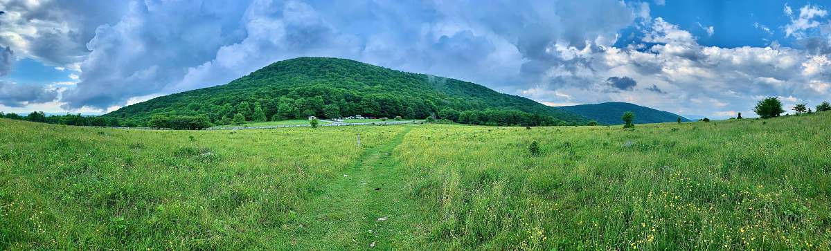 outdoors green grass field near green mountain under white clouds and blue sky during daytime field