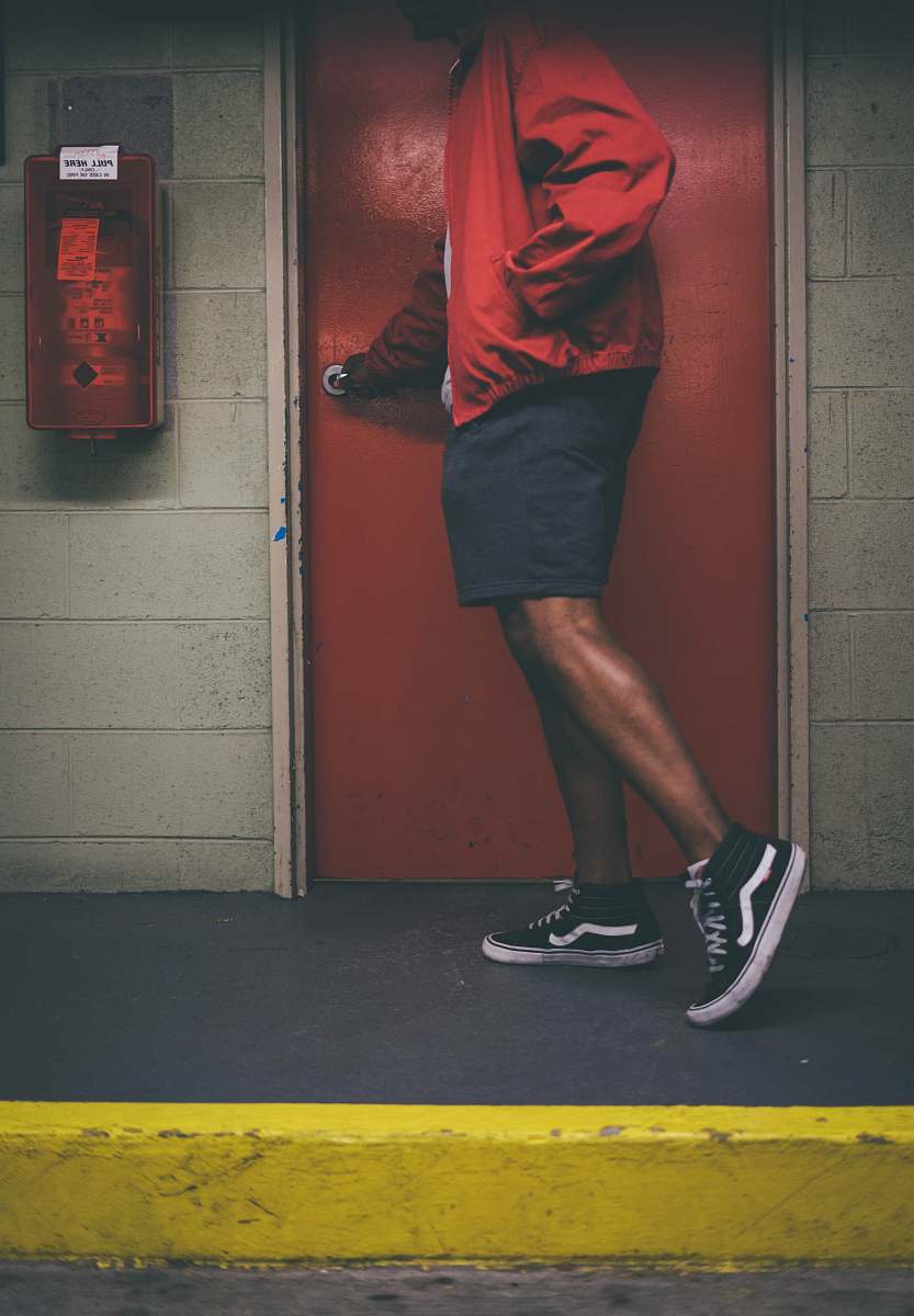 person man wearing red jacket holding door knob near red wooden door people