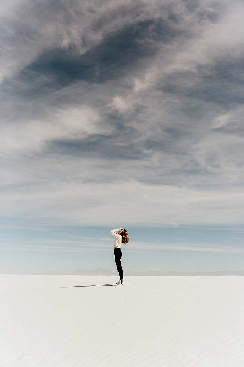 woman woman looking up to the sky while standing on white sand minimal