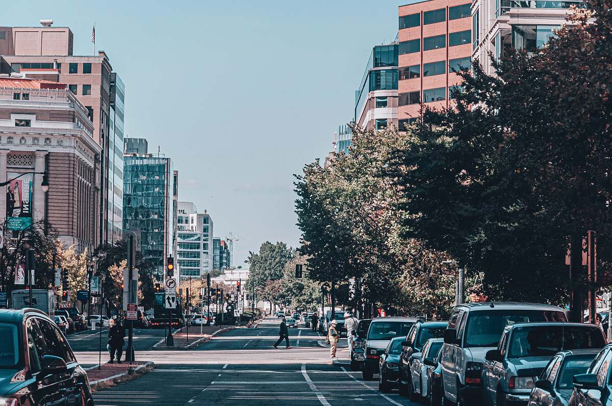 city cars parked on sidewalk near high rise buildings during daytime human