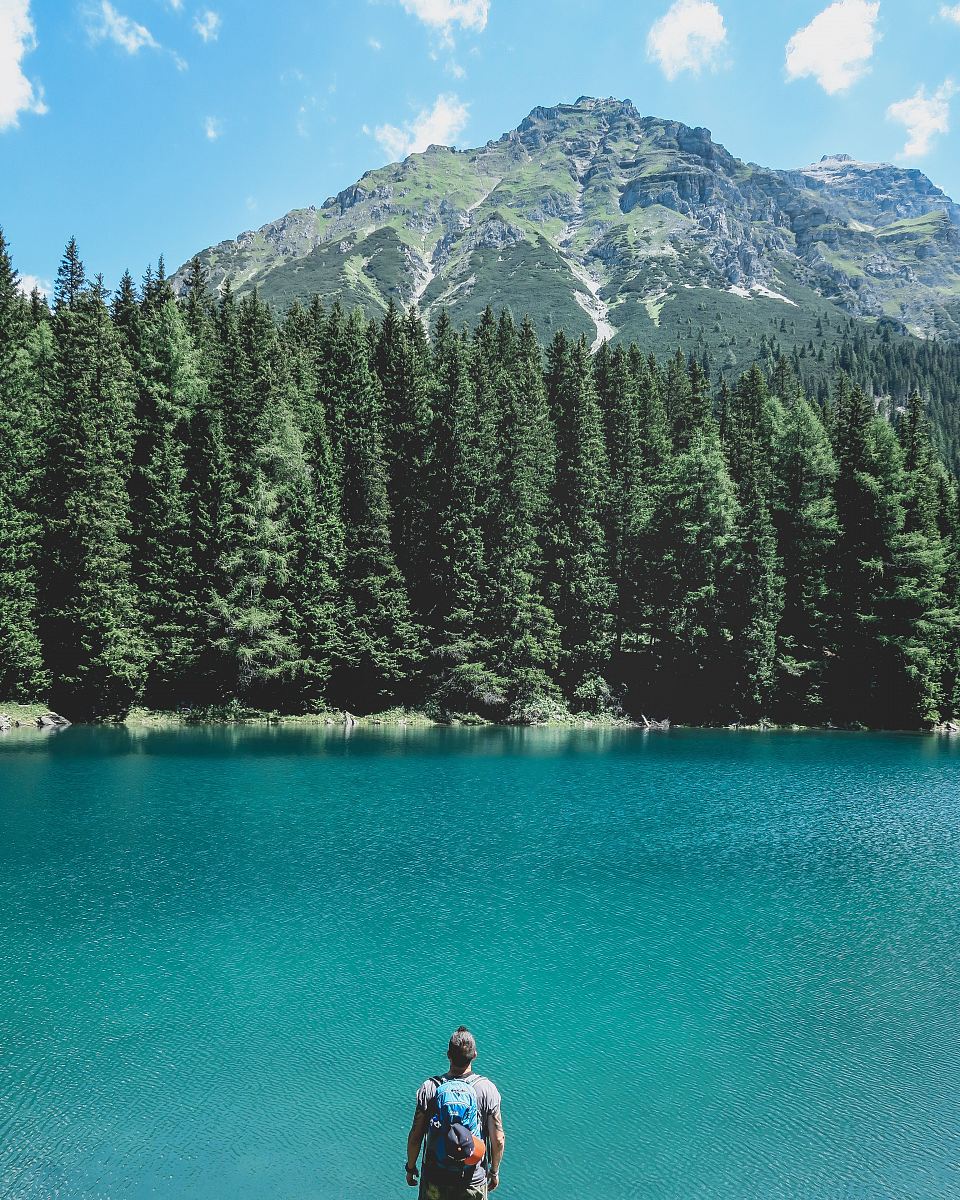 man looking through on lake with pine trees under blue sky
