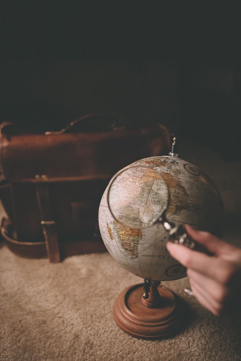 person holding magnifying glass near desk globe