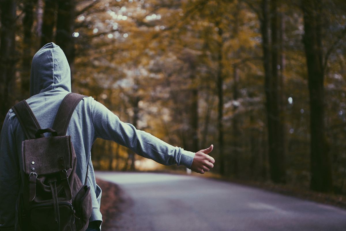 person standing beside road doing handsign
