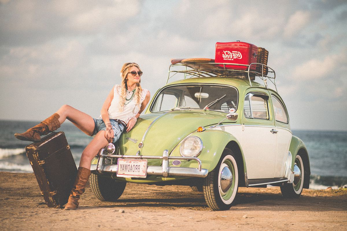 woman leaning on green and white Volkswagen Beetle near sea under white sky during daytime