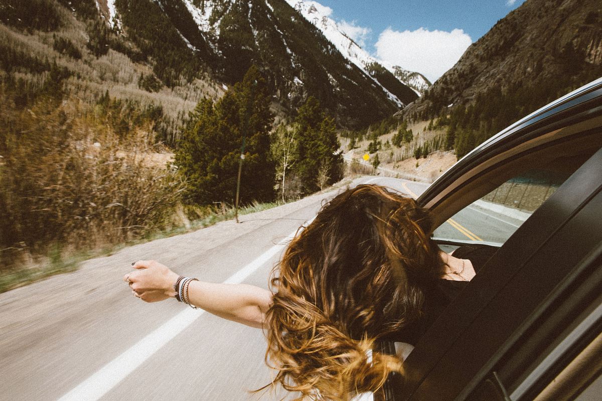 woman riding on vehicle putting her head and right arm outside the window while travelling the road