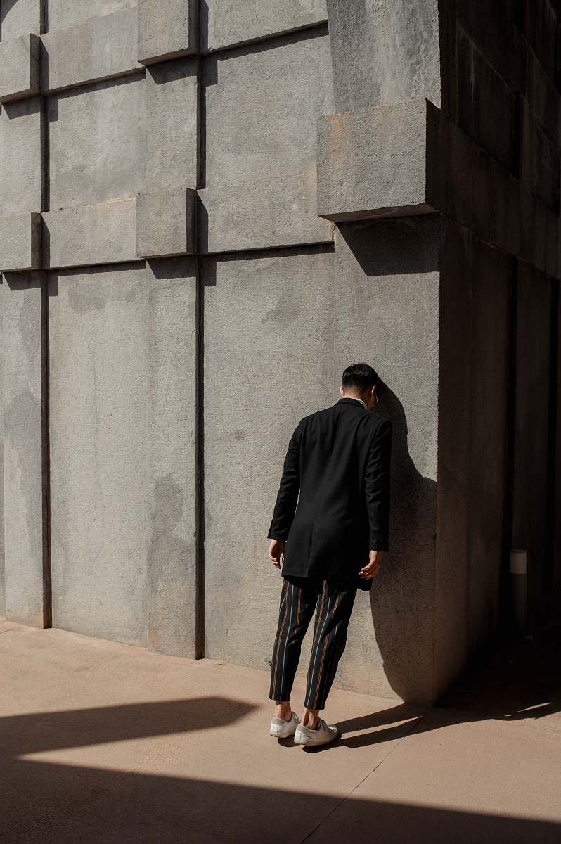 apparel man in black suit banging his head on wall overcoat