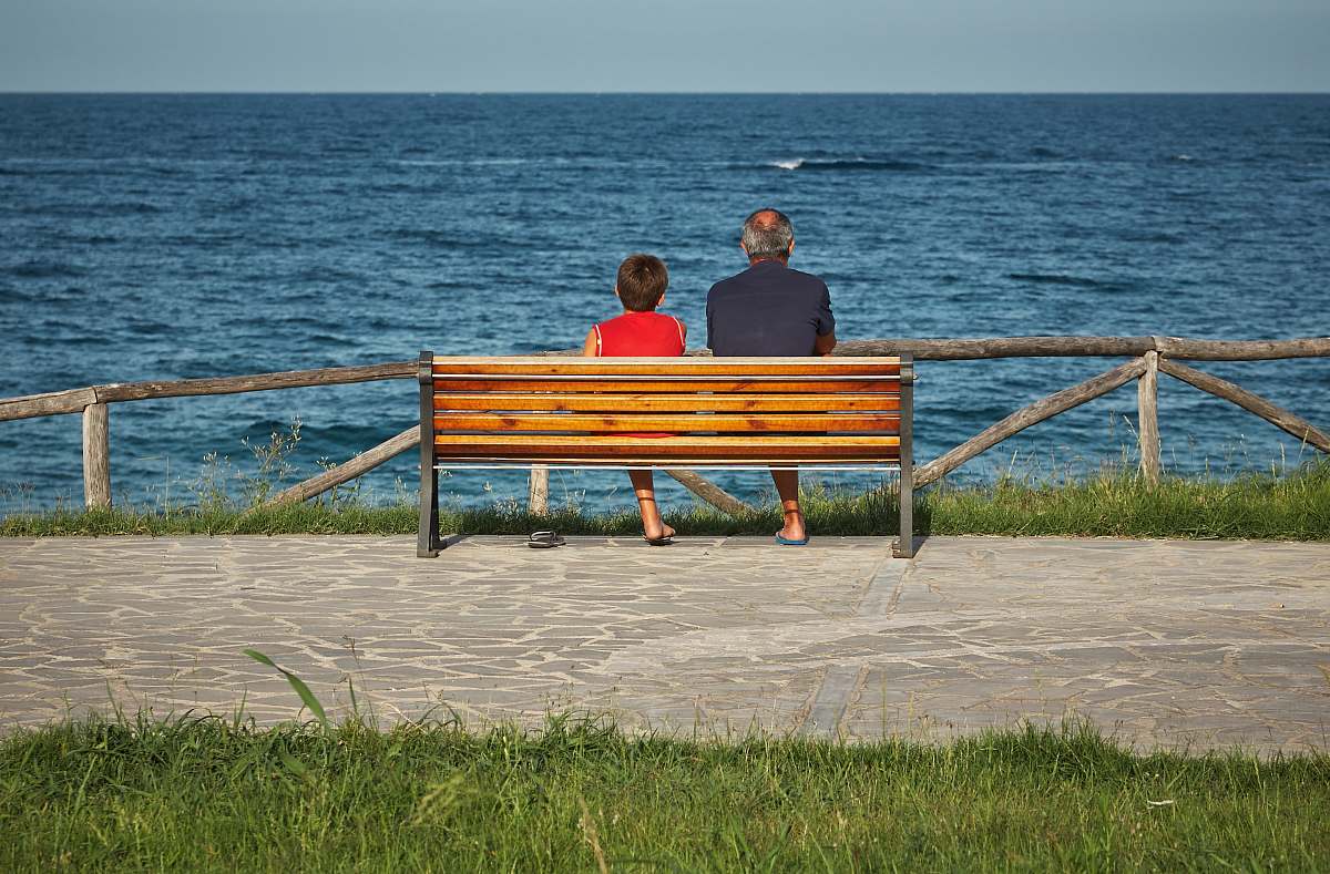 human two person sitting on bench beside body of water person