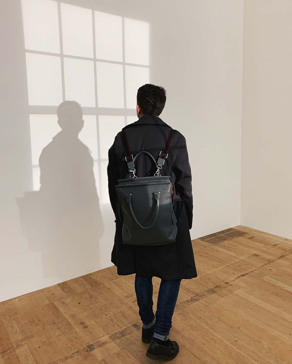 clothing man wearing black leather backpack standing near the wall apparel