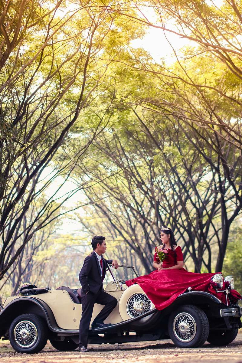 Capture the essence of romance with this enchanting image of a bride and groom seated in a classic vintage car, elegantly framed by a backdrop of vibrant trees. This picturesque scene is perfect for wedding invitations, romantic blog posts, or advertising nostalgic wedding themes. The vintage car adds a touch of timeless elegance, making it an ideal choice for photographers and marketers looking to evoke feelings of love and nostalgia.
