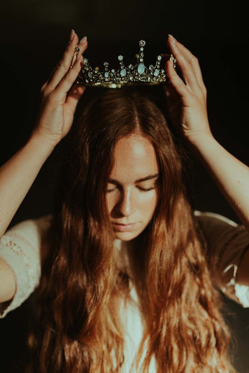 person woman putting silver-colored tiara on her head royal