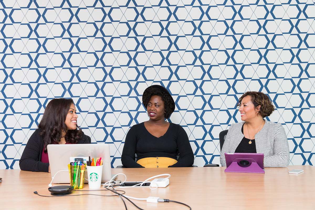 human three women sitting on chairs front of table sitting