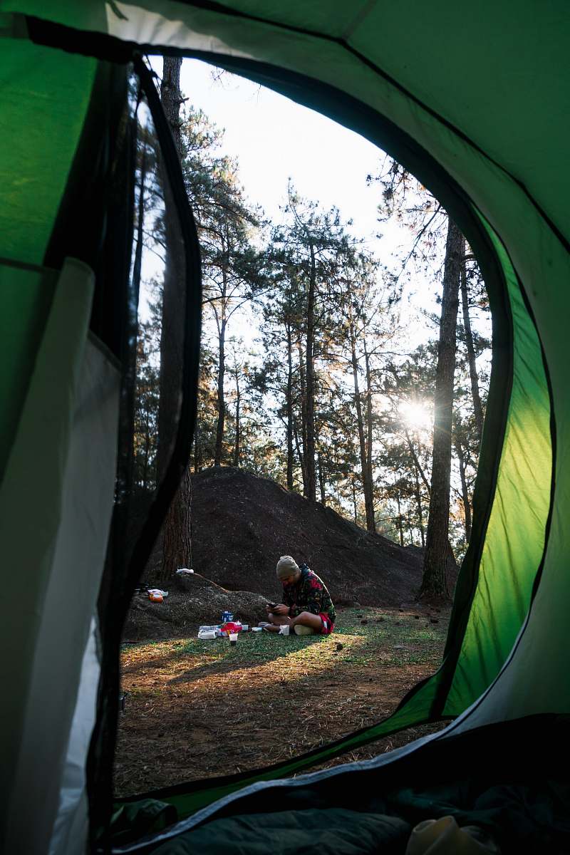 camping man sitting on grass surrounded by trees during daytime tent