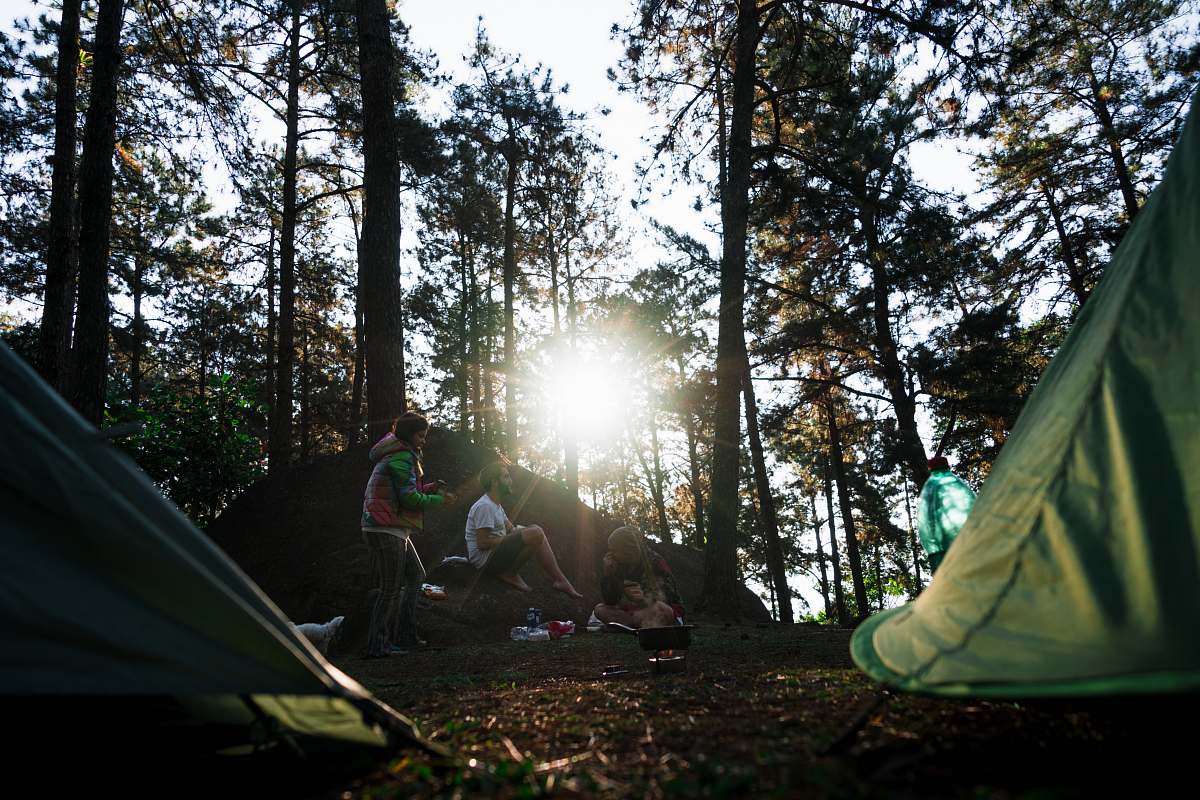 camping people sitting beside green dome tents during daytime leisure activities