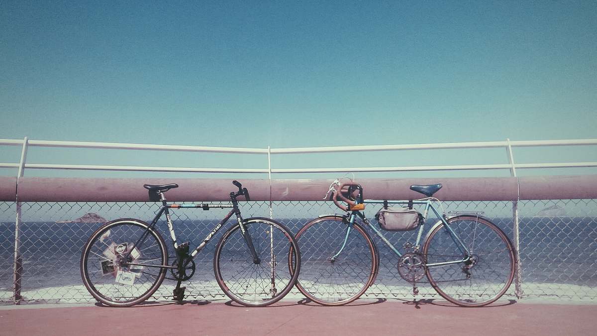 bicycle two black and gray bicycles parked near fence on seashore at daytime bike