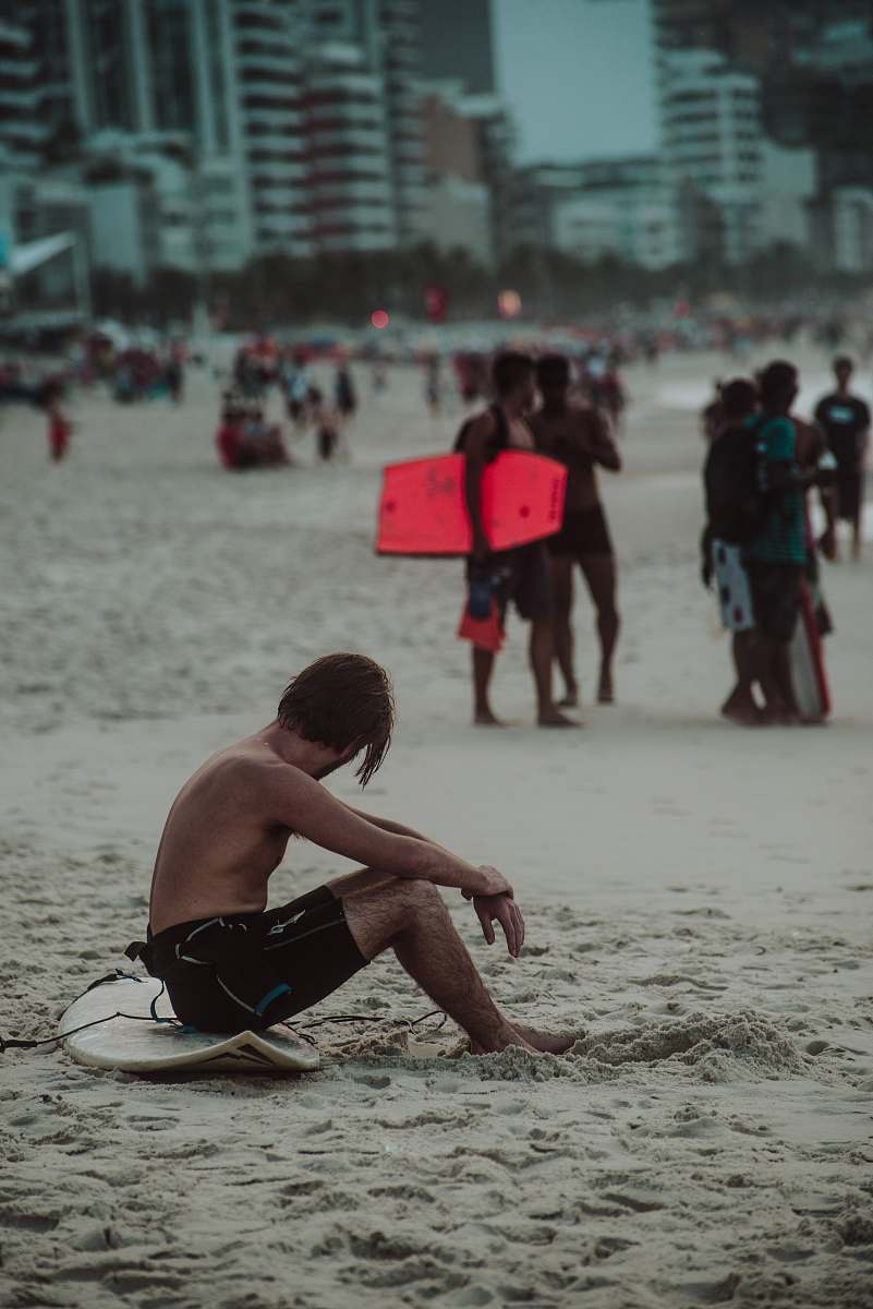 person man sitting on white surfboard on sand during daytime back