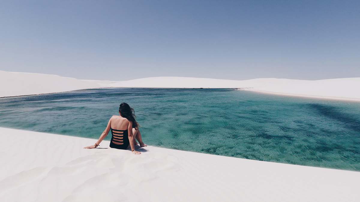 person woman sitting on white sand near body of water people