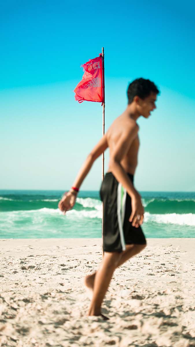 ocean selective focus photo of red flag on brown pole near body of water beach