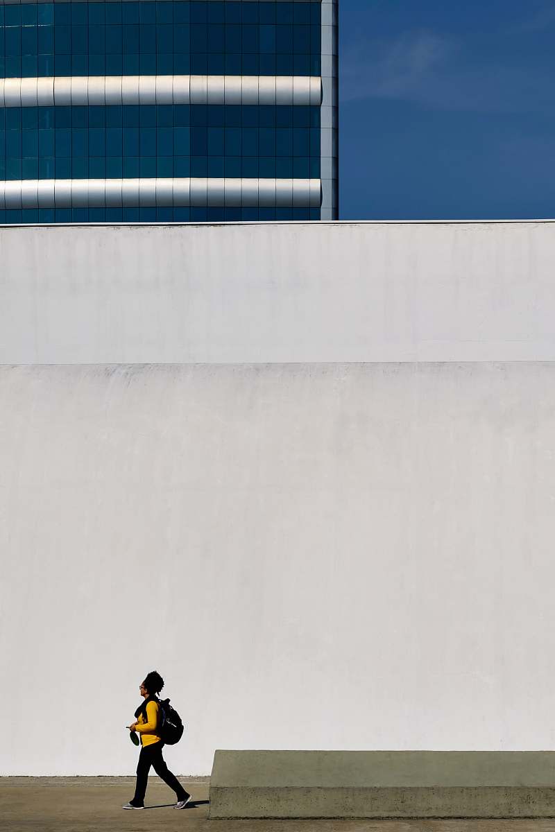 people human in yellow long-sleeved T-shirt walking beside white concrete wall human