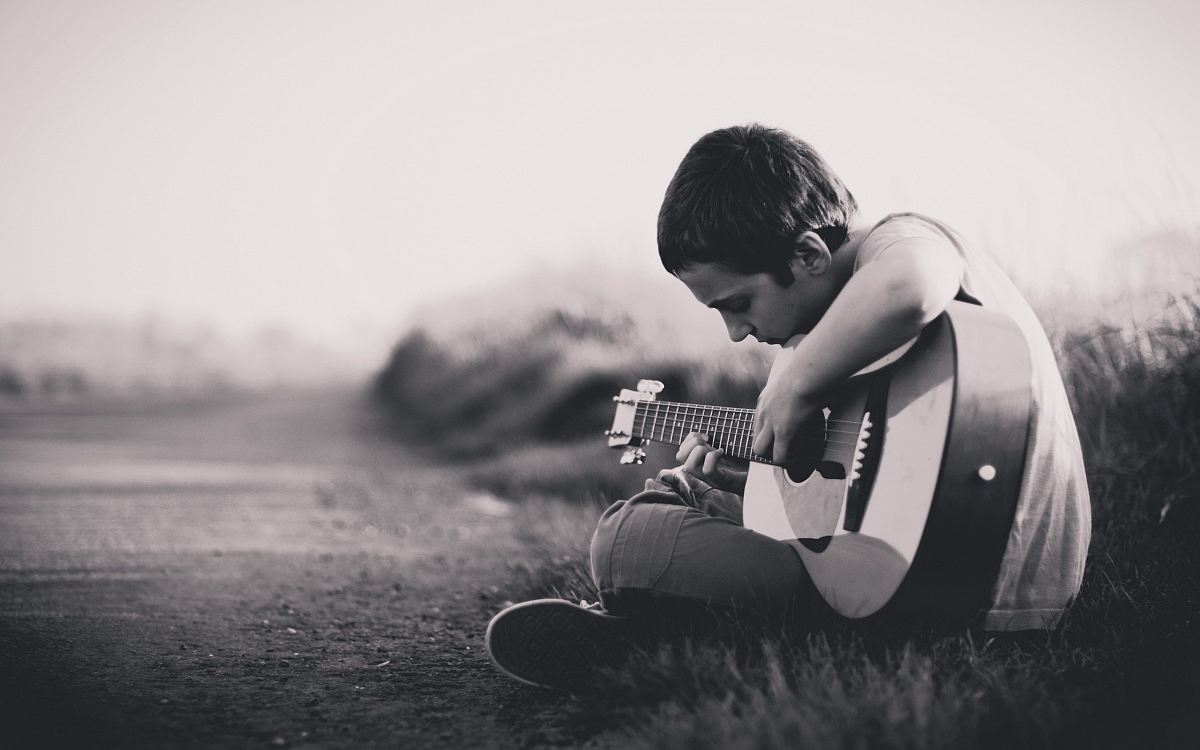 grayscaled photo of boy playing guitar