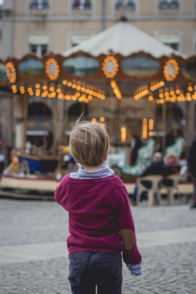 selective focus photography of boy standing in front of carousel