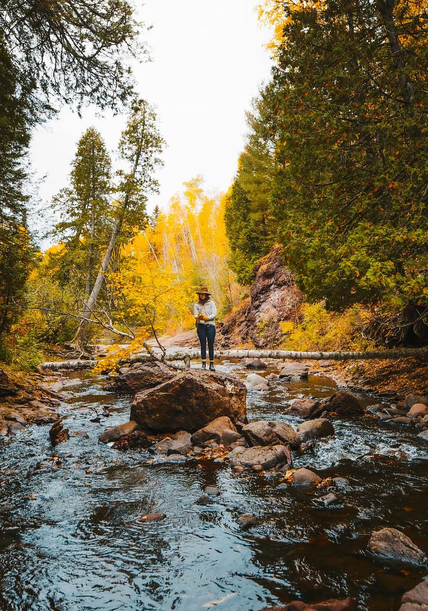 outdoors woman in white jacket standing on rock in river during daytime nature