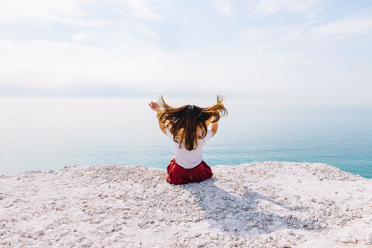 woman sitting on cliff near body of water