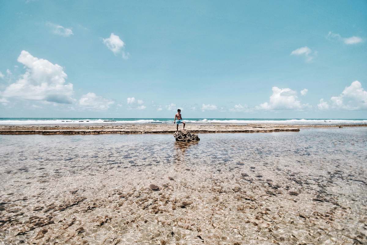 coast person standing on rock surrounded by body of water ocean