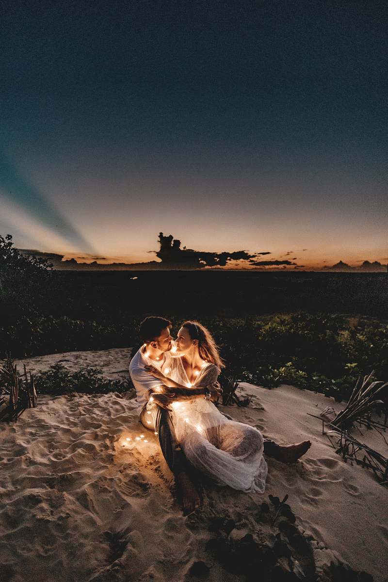Capture the essence of romance with this stunning image of a couple gazing into each other's eyes while seated on pristine white sand during a captivating sunset. The warm hues of the setting sun create a magical backdrop, perfect for love-themed projects, travel brochures, or social media content. This serene moment encapsulates the beauty of nature and human connection, making it an ideal choice for wedding themes, relationship blogs, or inspirational quotes.