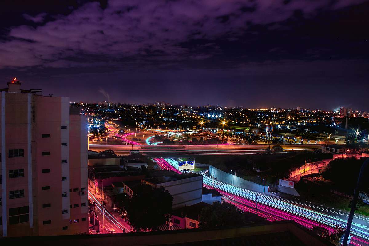 city timelapse photography of vehicle passing on road under cloudy skies at night time urban