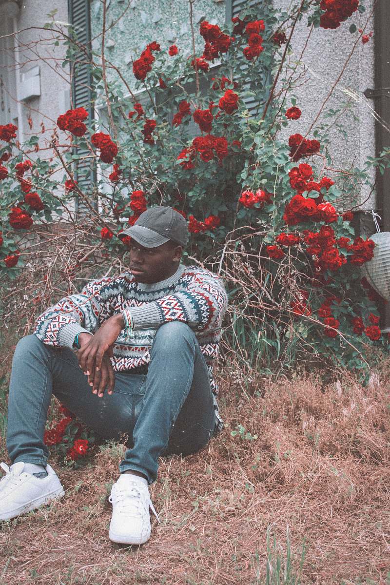 human man sitting on grass in front of red flowered plant person