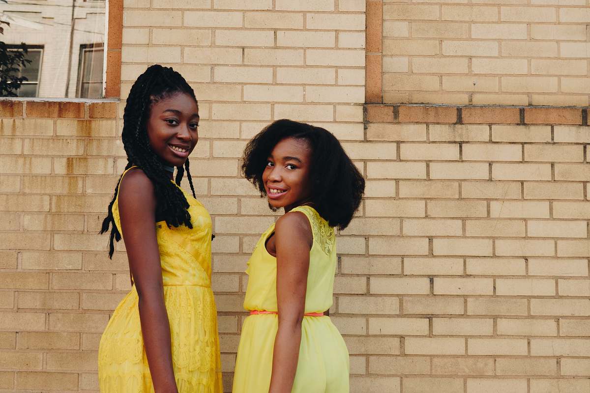 human two women wearing yellow sleeveless dresses near brown brick people