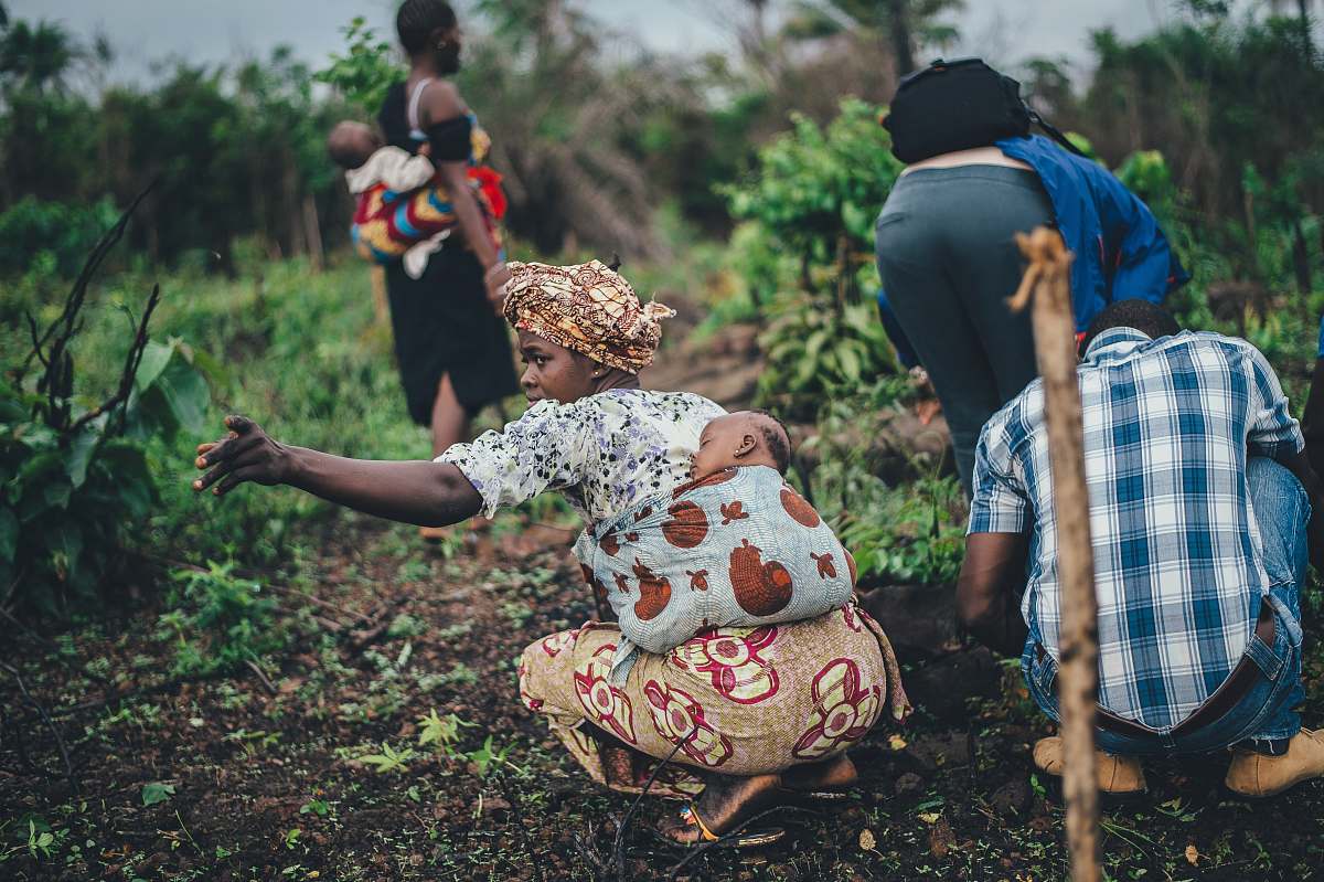 human woman carrying toddler at back while planting people