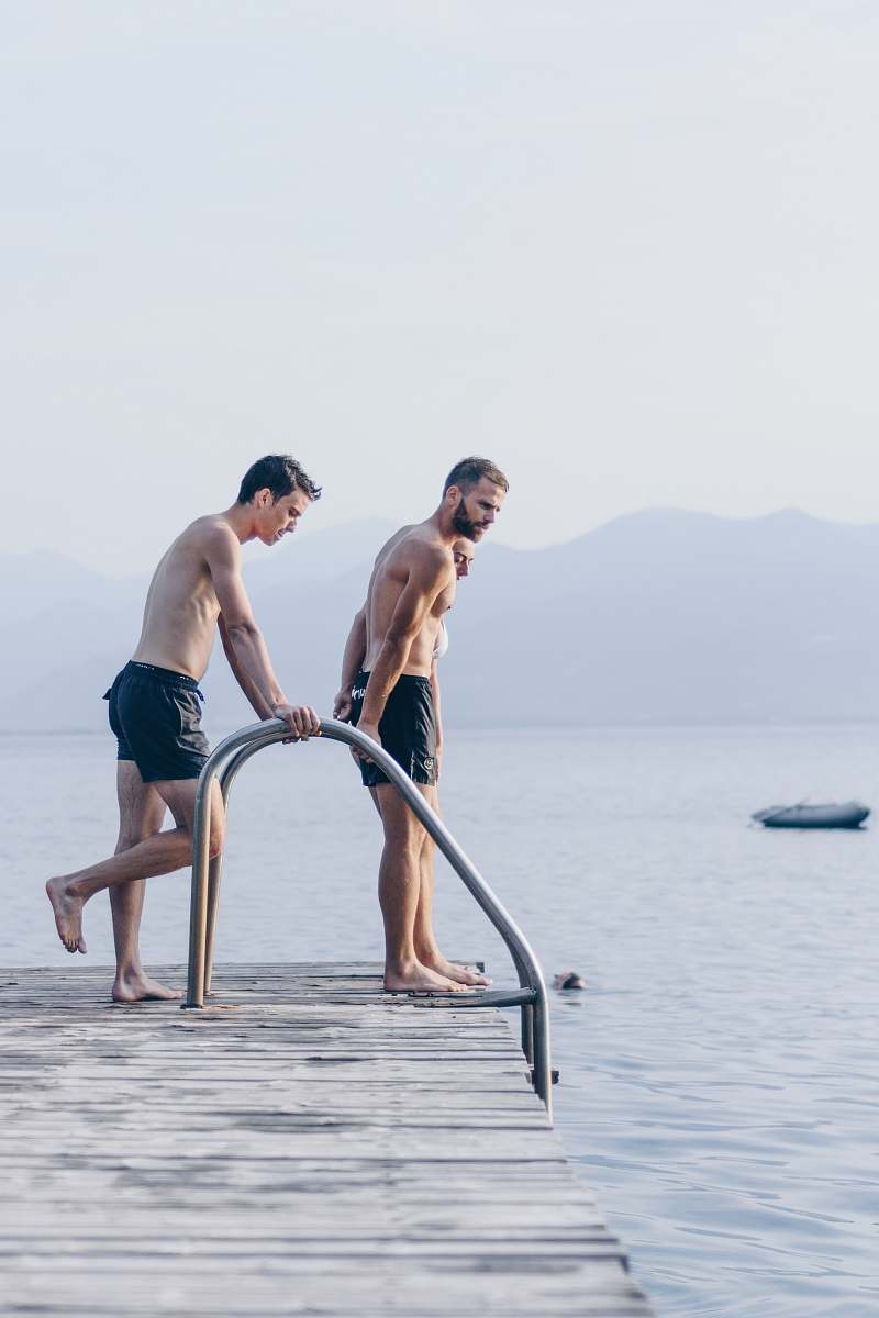 person two men standing on brown dock near body of water during daytime people