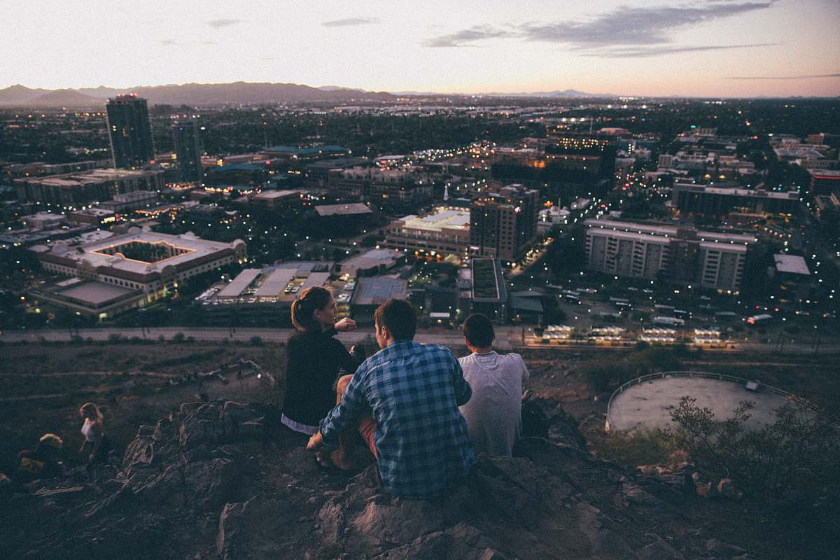 Capture the essence of camaraderie and adventure with this stunning image of three individuals perched on a cliff, gazing out over a sprawling city. The scene beautifully blends nature with urban life, making it perfect for travel blogs, lifestyle articles, or promotional content for outdoor activities. The juxtaposition of the serene hilltop and the vibrant city below creates a compelling visual narrative that invokes feelings of exploration and togetherness.