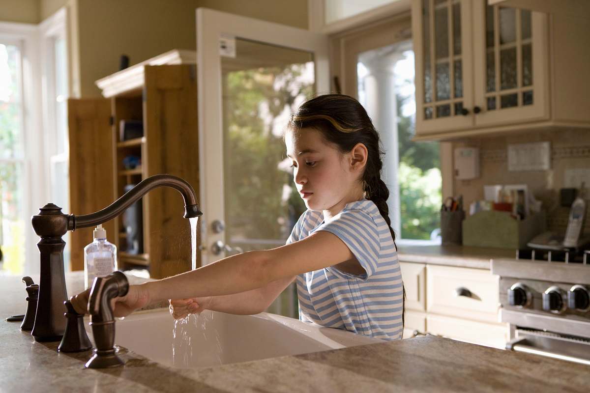 human woman in blue and white stripe shirt washing her hands sink