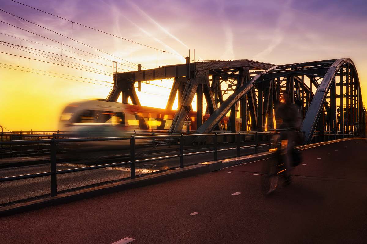 architecture time-lapse photography of biker passing road beside trail during golden hour bridge